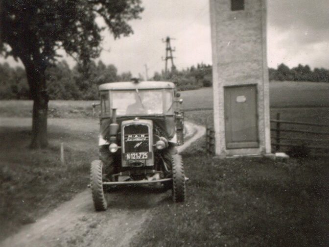 Ein Traktor fährt auf einem Feldweg umgeben von Wiesen.