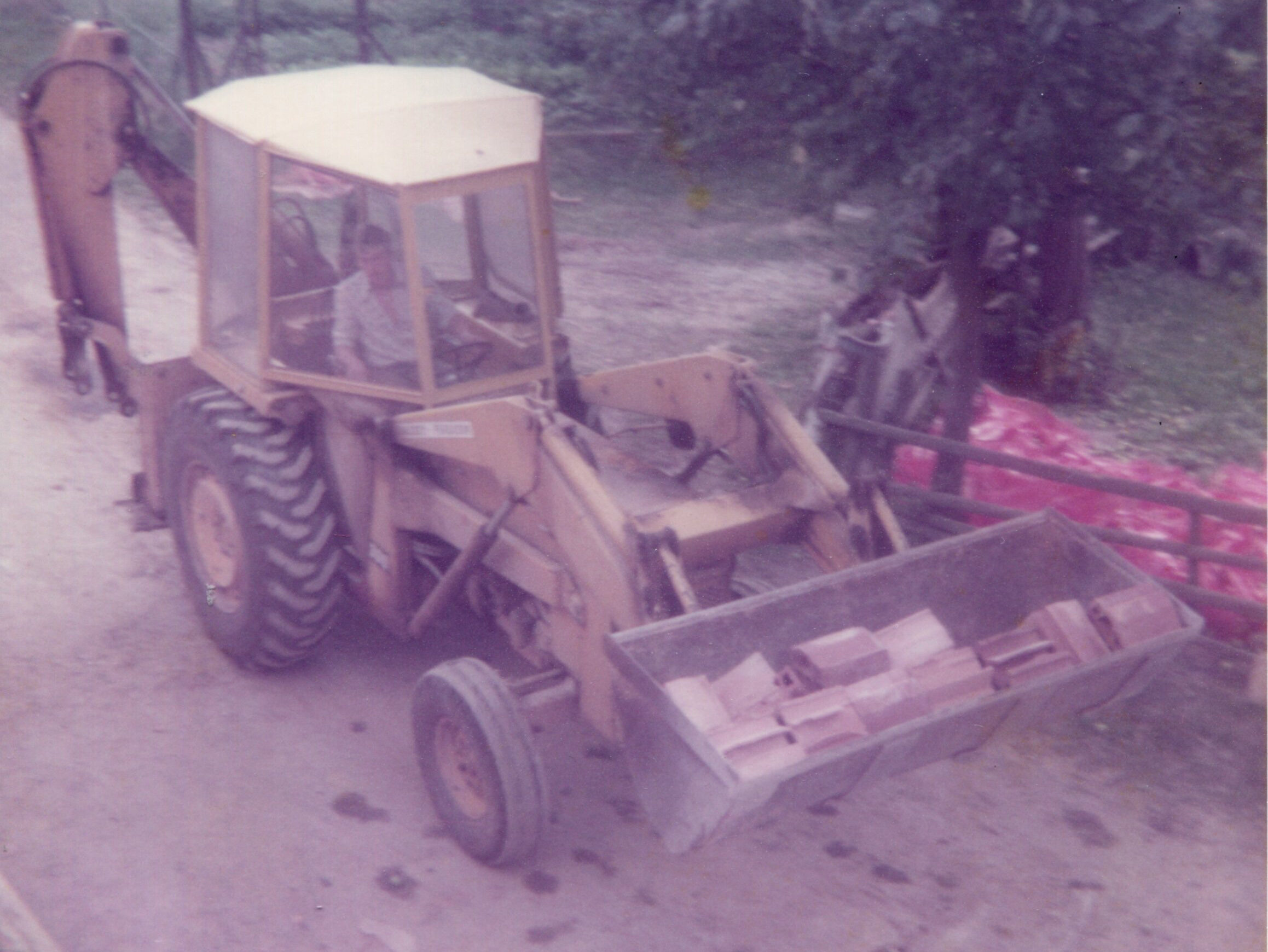 Ein gelber Bagger älteren Baujahrs fährt mit Ziegeln in der Schaufel. 