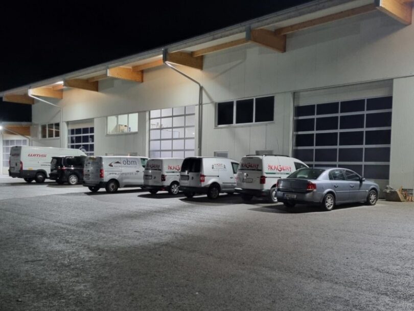 Mehrere Firmen-Pkws parken nachts vor einer Gewerbehalle mit großen Einfahrtstoren. 