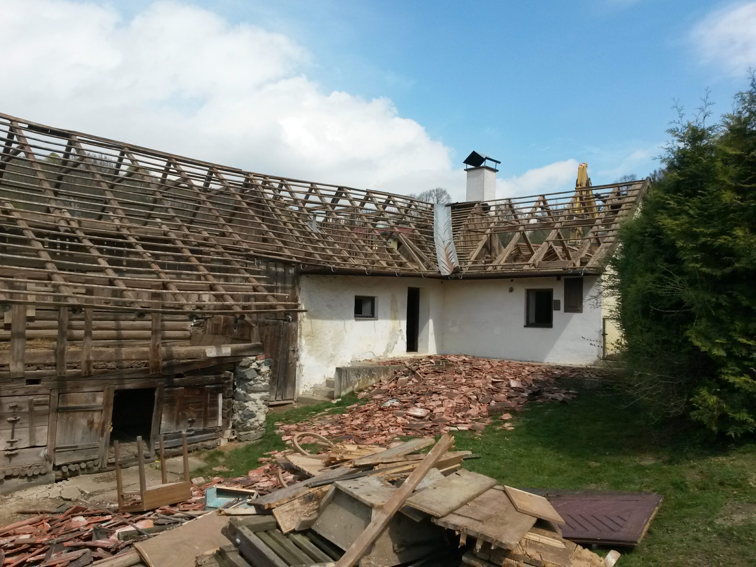 Hofansicht eines Gebäudes mit komplett abgedecktem Dach und freiliegendem Dachstuhl; im Vordergrund liegen abgetragene Dachziegel und Holzreste, blauer Himmel mit Wolken.