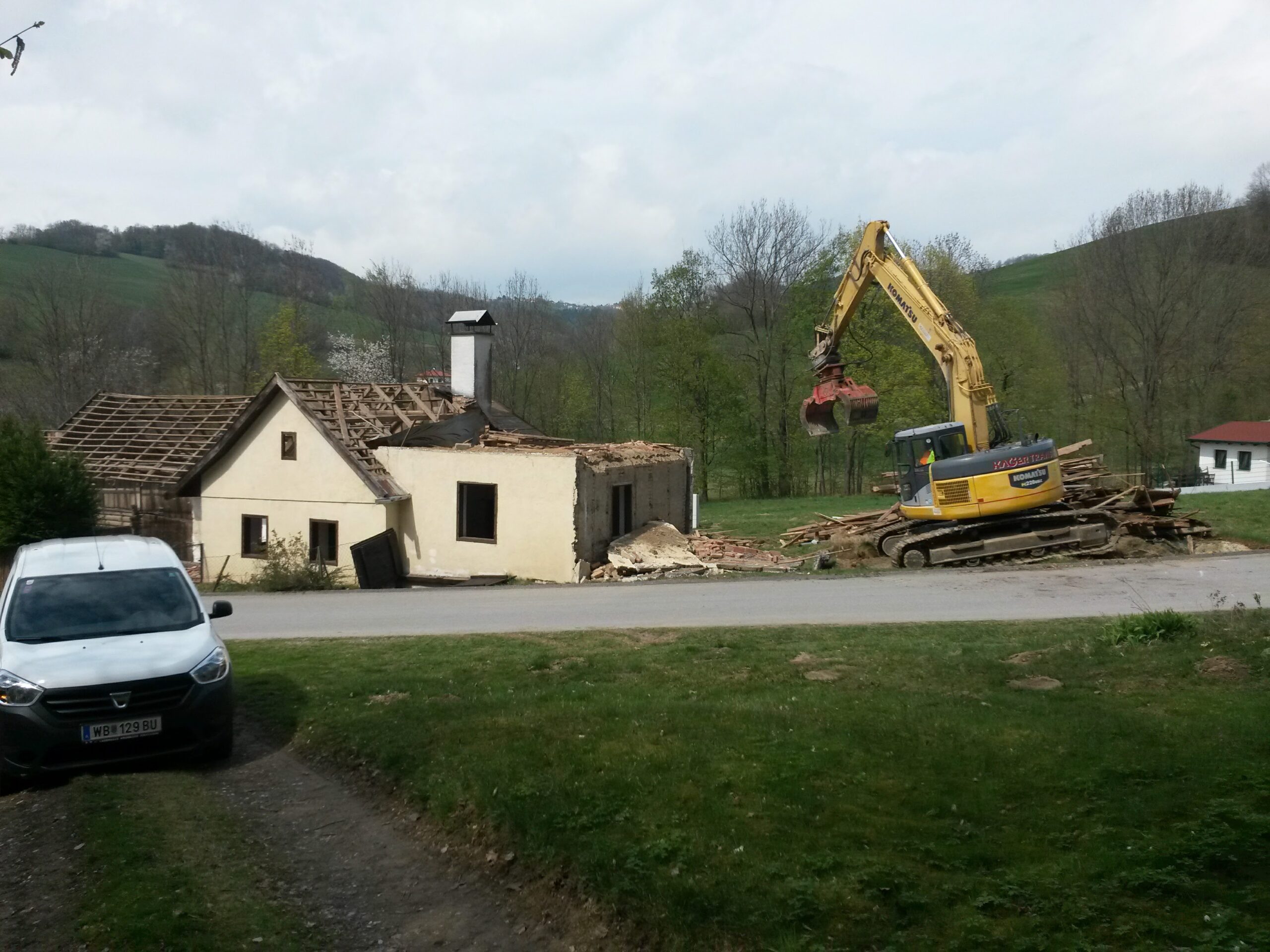 Einfamilienhaus in Alleinlage wird von einem gelben Bagger abgerissen. 