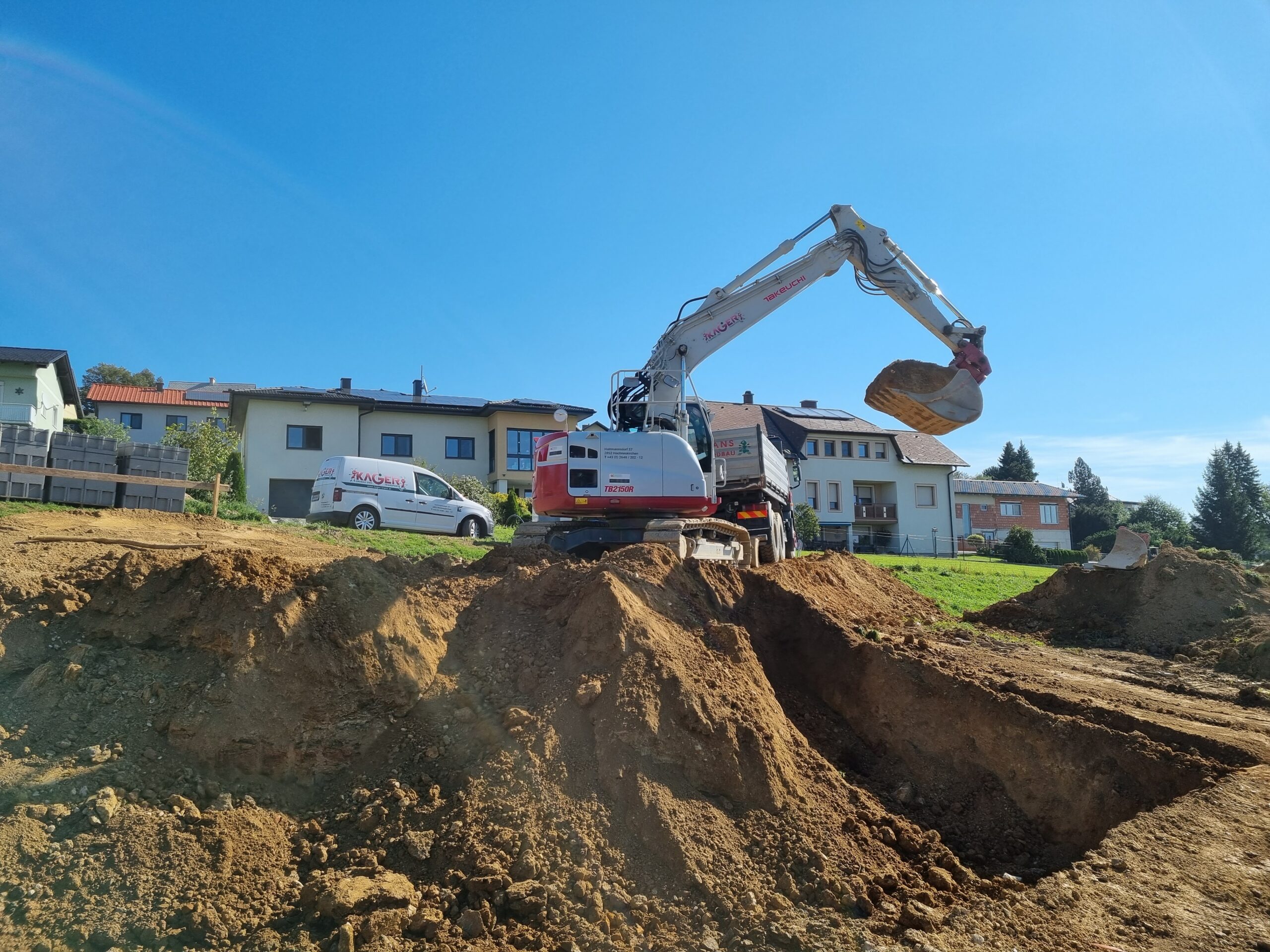 Bagger mit erhobenem Greifarm hebt Erde aus Baugrube aus.