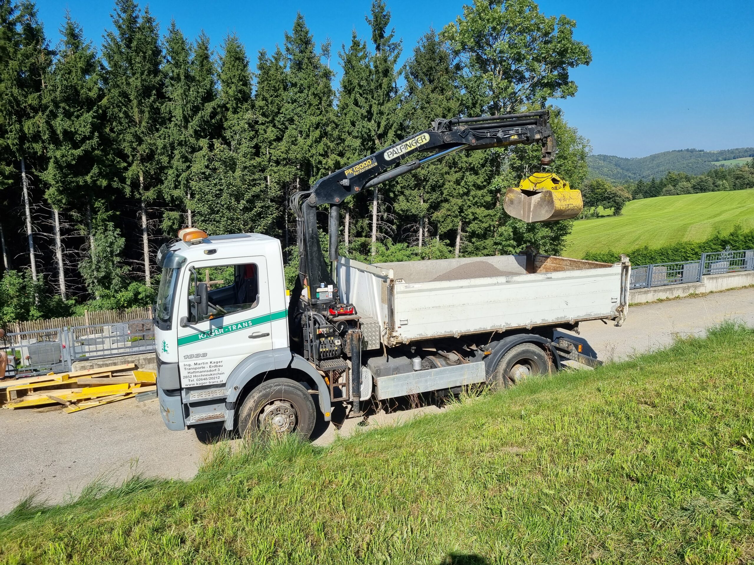 Lkw-Kipper mit Palfinger-Kran hebt eine Greifschaufel über die Ladefläche.
