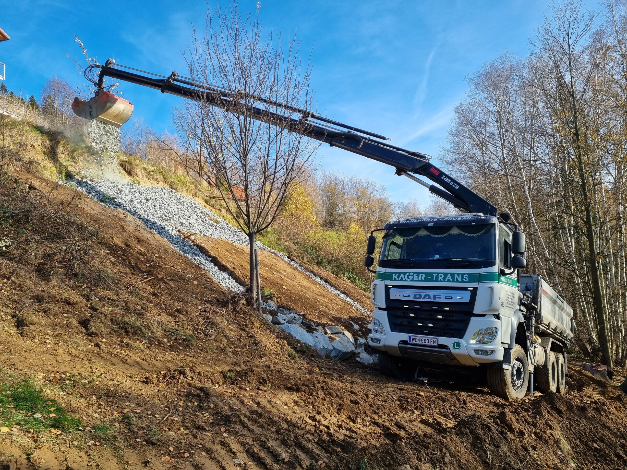DAF-Kipper mit Auslegerkran schüttet Schotter auf einen Hang.