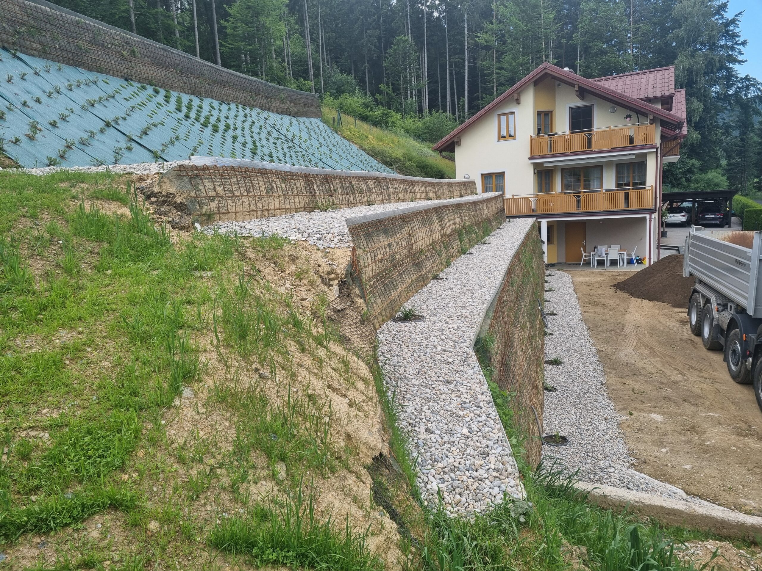 Gesicherter Hang in mehreren Ebenen und mit bewehrter Erde vor einem Einfamilienhaus. 