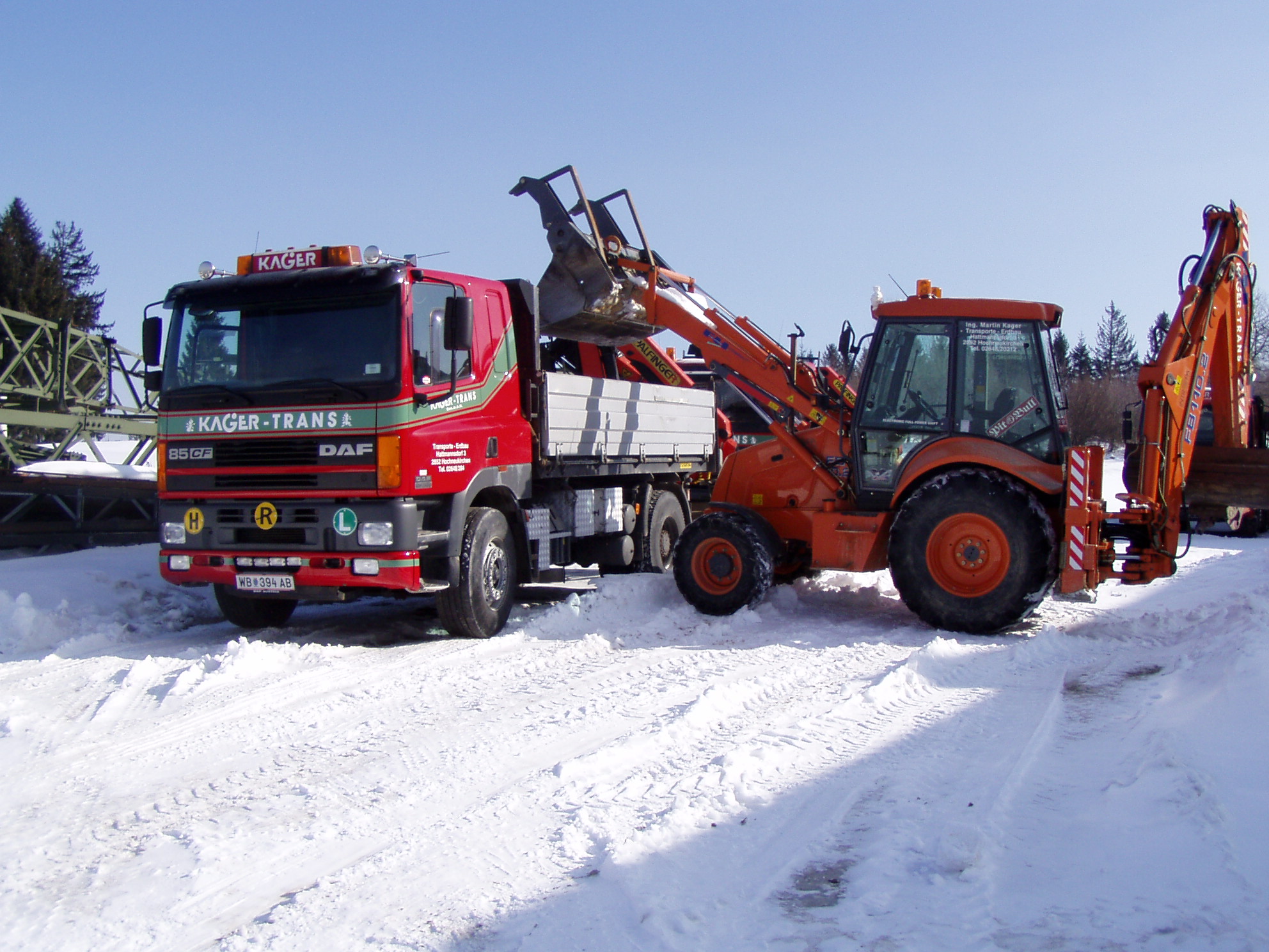 Ein Bagger lädt Schnee im Winter auf einen roten Lkw.